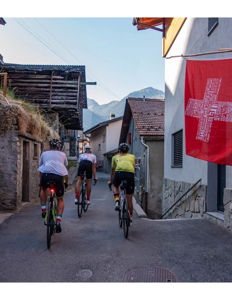 kolarze jadą po szwajcarskiej wiosce ubrani w stroje Luxa i skarpetki z flagami różnych państw
