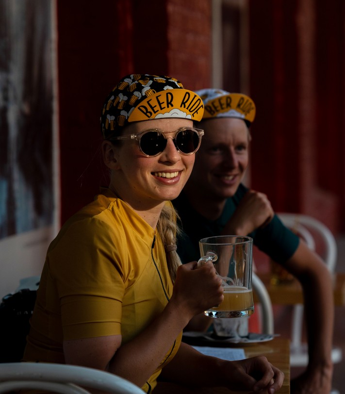 dziewczyna pije bezalkoholowe piwo i nosi rowerową czapeczkę Luxa Beer Ride