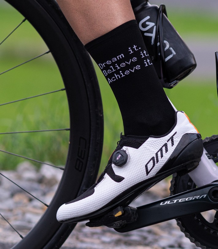 left leg of road cyclists who is wearing DMT shoes and Luxa socks with message on one side