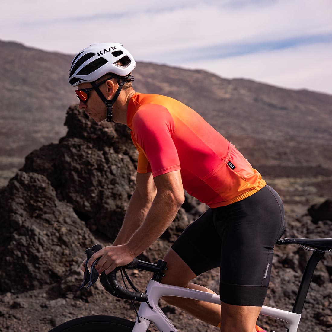 kolarz ubrany w pomarańczowy str&oacute;j rowerowy jedzie pod wulkanem Teide