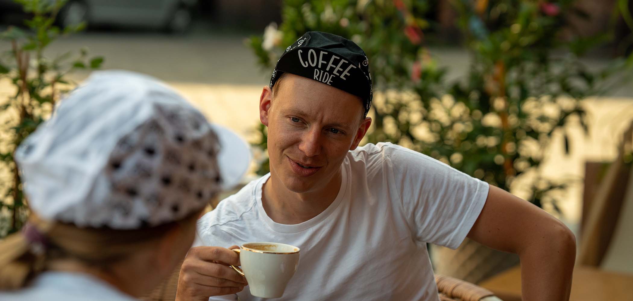 a man sits at a table drinking coffee and wears a cap with the inscription &#039;coffee ride&#039;