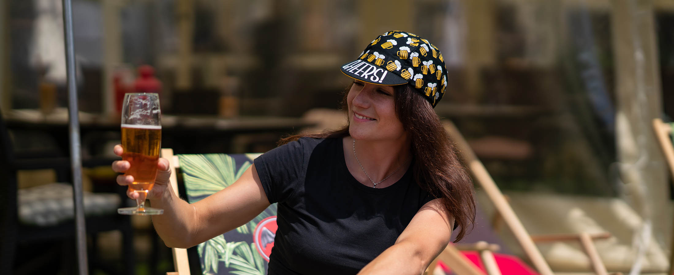 a woman holds a non-alcoholic beer and wears a &#039;beer ride&#039; cap with the word &#039;cheers&#039; on top of the peak