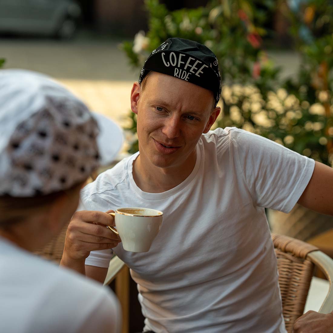 mężczyzna siedzi przy stoliku pijąc kawę i nosi czapeczkę z napisem &#039;coffee ride&#039;